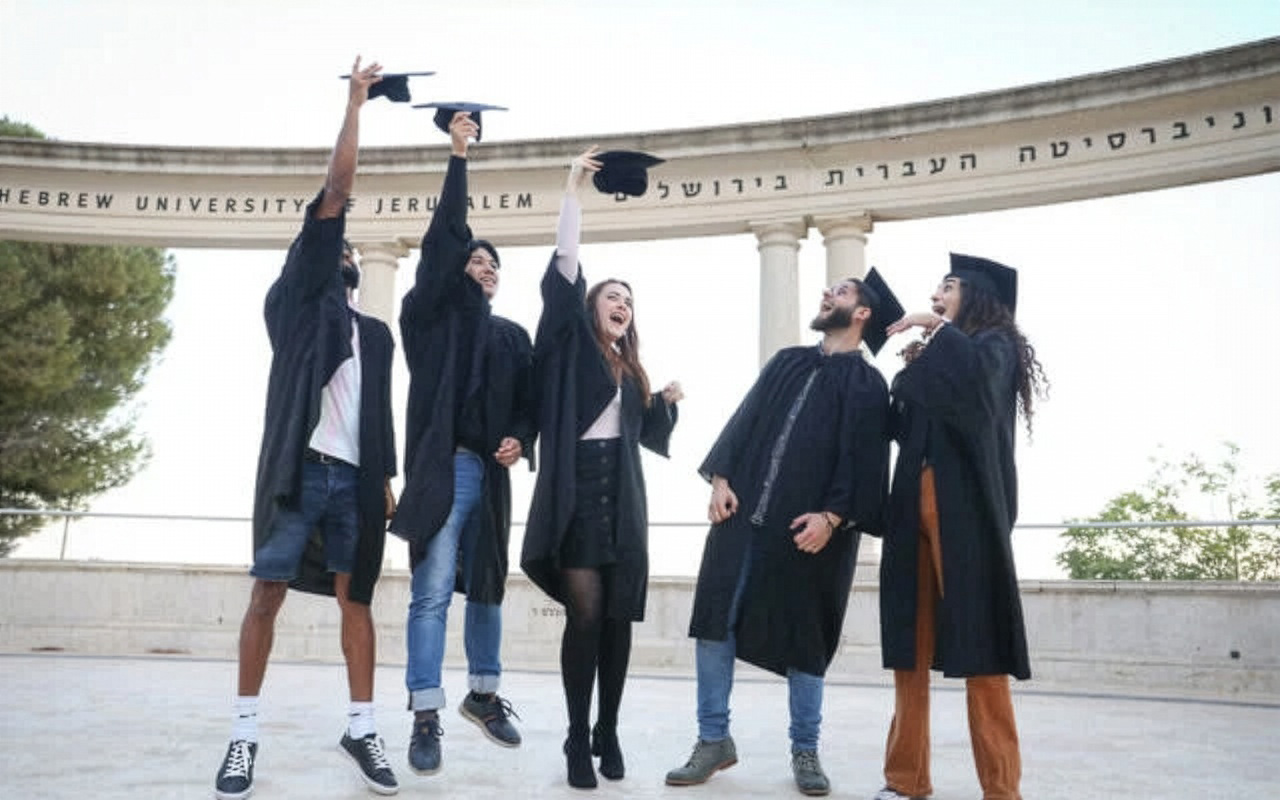 Fünf jubelnde Absolventinnen und Absolventen in schwarzen Talaren werfen an der Hebrew University of Jerusalem ihre Doktorhüte in die Luft.